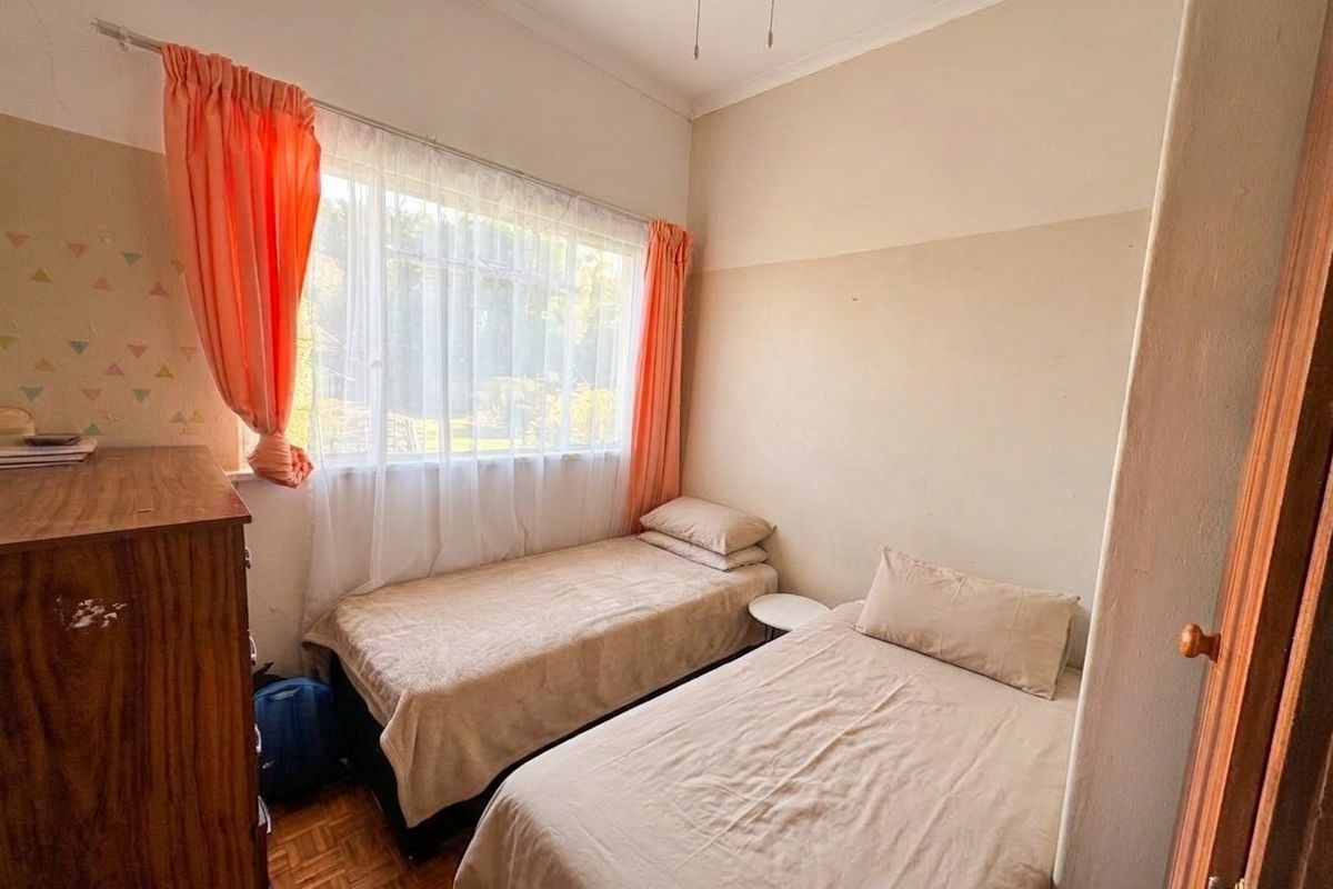 A bedroom featuring parquet flooring, a ceiling fan, and a large window, currently showing signs of wear on the walls.