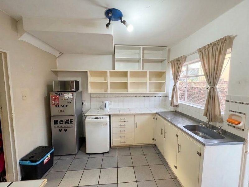 A functional kitchen featuring tiled countertops, built-in cabinetry, and a stainless steel sink, offering potential for modernization and cosmetic updates.