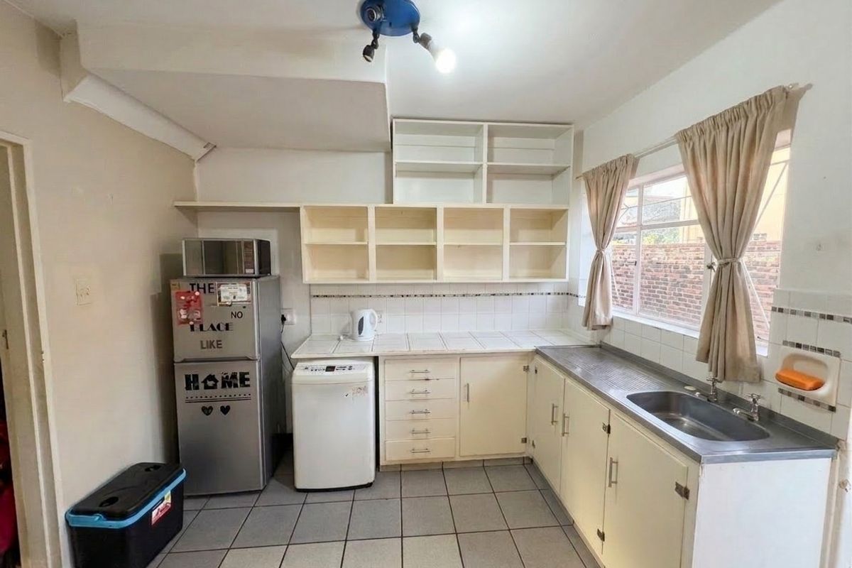 A functional kitchen featuring tiled countertops, built-in cabinetry, and a stainless steel sink, offering potential for modernization and cosmetic updates.