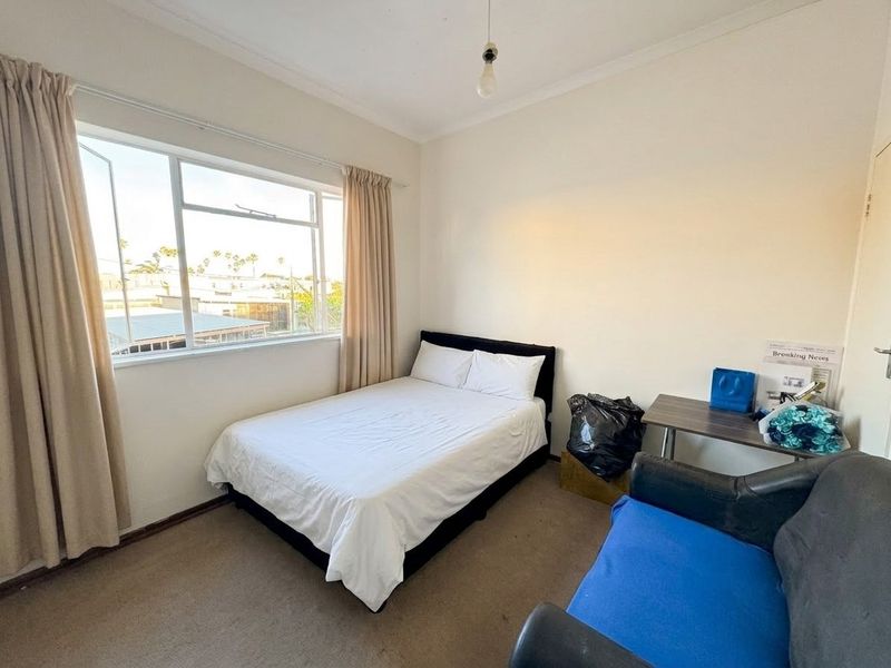 A functional bedroom featuring a large window, carpeted flooring, and coved ceilings, offering a blank canvas for potential updates and modernization.