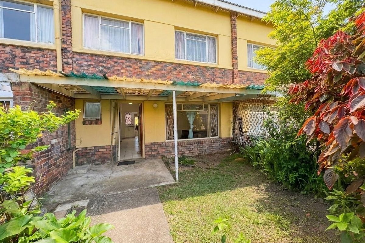 Rear view of a townhouse featuring a brick facade, a small patio area with a pergola, and a private garden space.