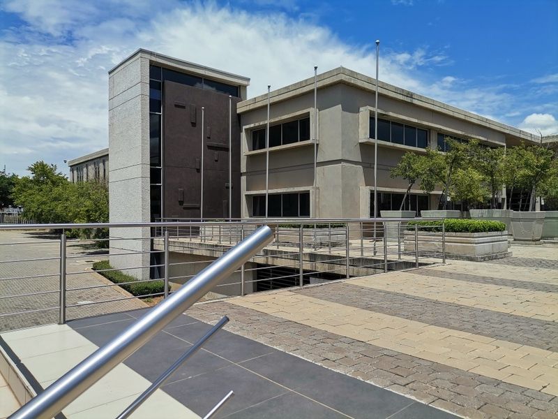 Modern commercial building exterior featuring a concrete facade, tinted windows, and a paved entrance walkway with stainless steel railings.
