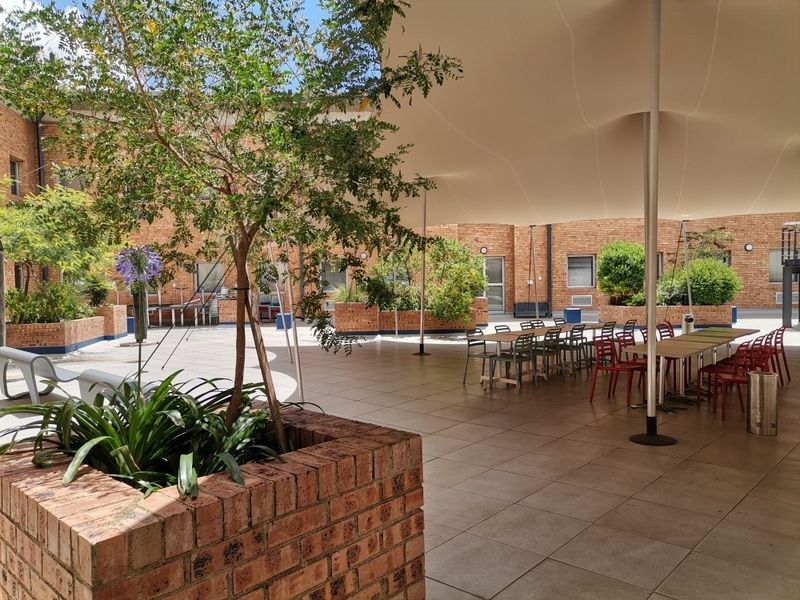 A spacious outdoor courtyard featuring tiled flooring, brick planter boxes, and a large tension fabric canopy providing shade for the commercial area.
