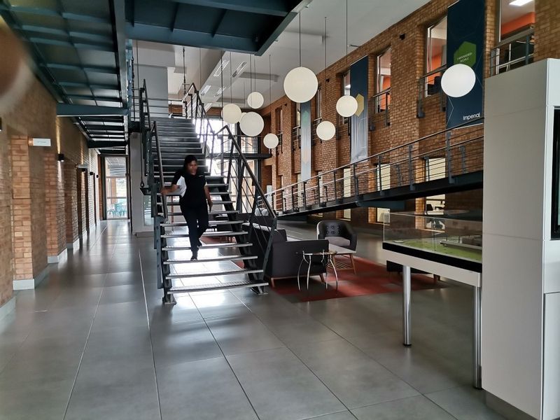 Spacious commercial lobby featuring an industrial aesthetic with exposed brick walls, tiled flooring, and a prominent metal staircase leading to a mezzanine level.