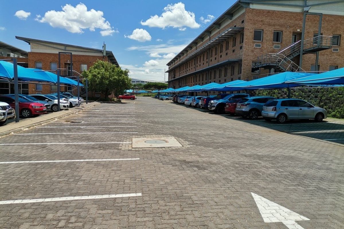 Commercial property exterior featuring a large paved parking area with blue shade cloth carports and multi-story brick office buildings.