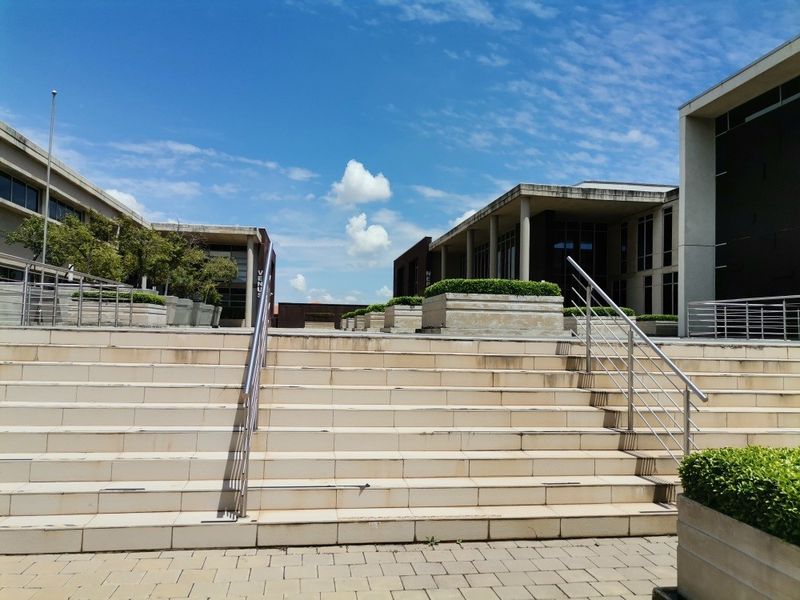 A wide stone staircase with stainless steel handrails leading to a commercial courtyard area with built-in planters and paved surfaces.
