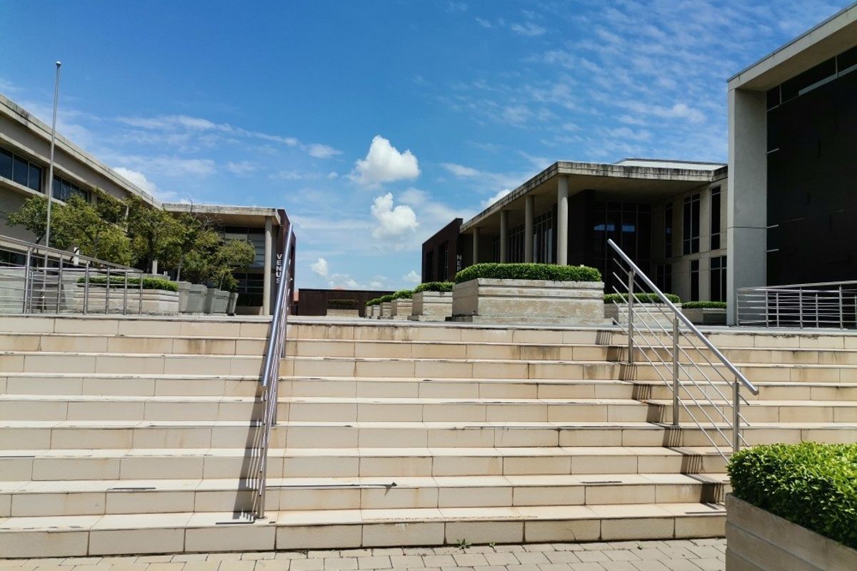 A wide stone staircase with stainless steel handrails leading to a commercial courtyard area with built-in planters and paved surfaces.