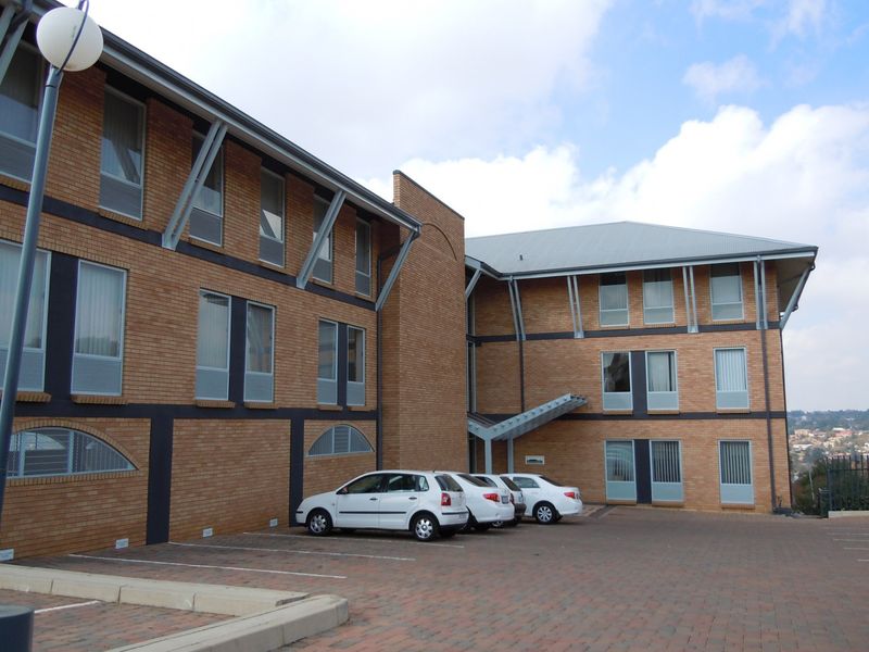 A multi-story commercial office building featuring a brick facade, metal roofing, and an adjacent paved parking area.