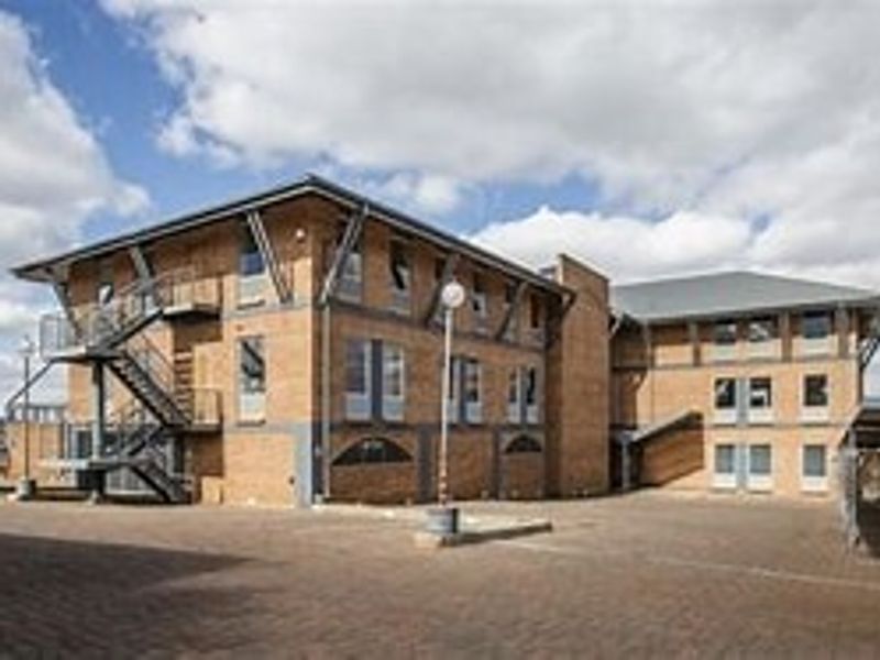 A multi-story commercial brick building featuring an external metal staircase and a paved courtyard area.