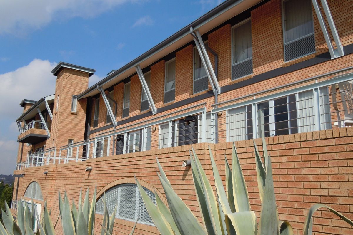 A multi-story commercial building featuring a face brick facade, steel balcony railings, and large sliding glass doors with metal structural supports.