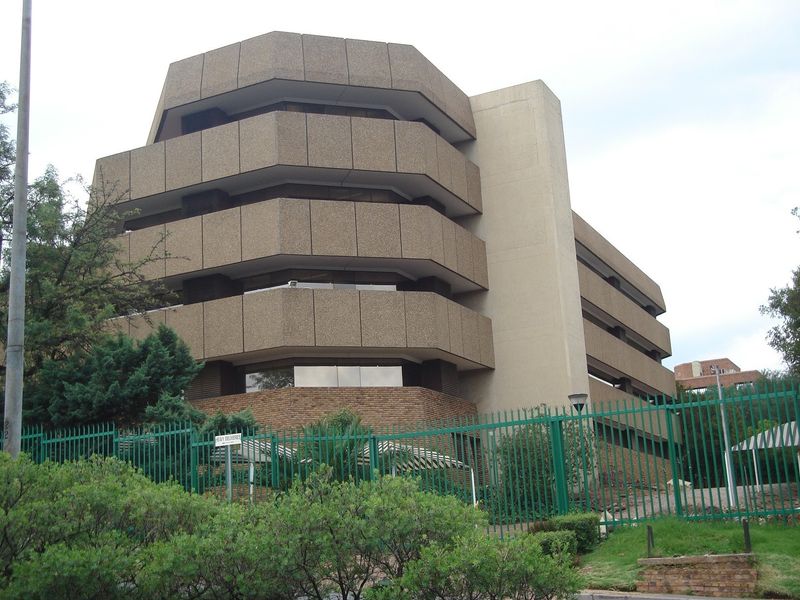 A multi-story commercial office building featuring a tiered concrete facade and secure perimeter fencing.
