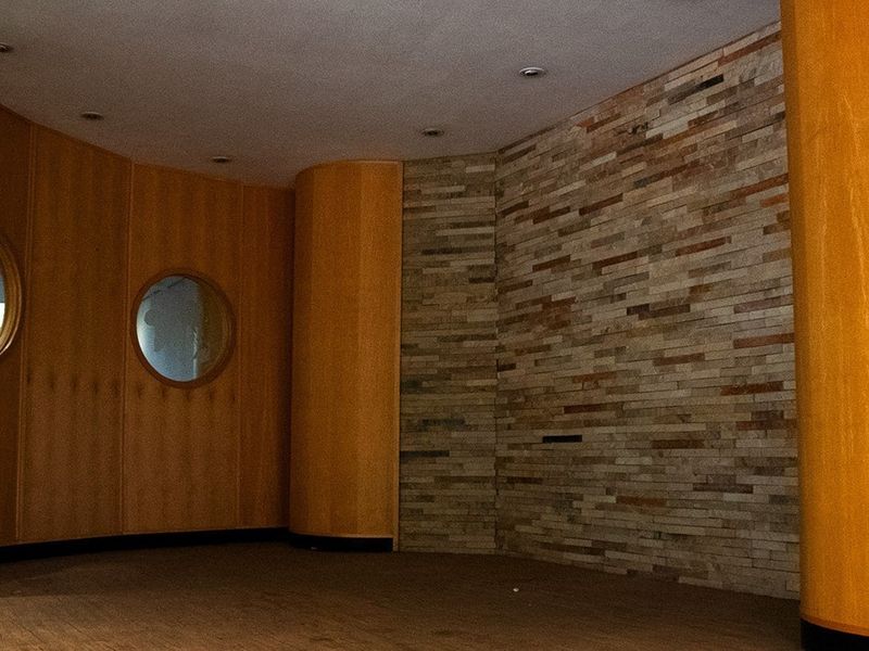 An empty commercial interior space featuring a combination of warm wood paneling, a textured stone feature wall, and unique circular window detailing.