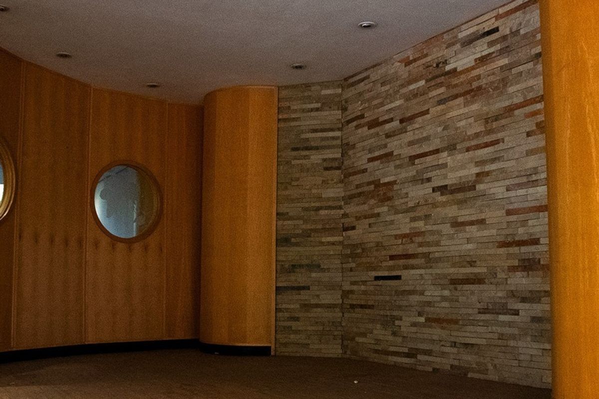 An empty commercial interior space featuring a combination of warm wood paneling, a textured stone feature wall, and unique circular window detailing.