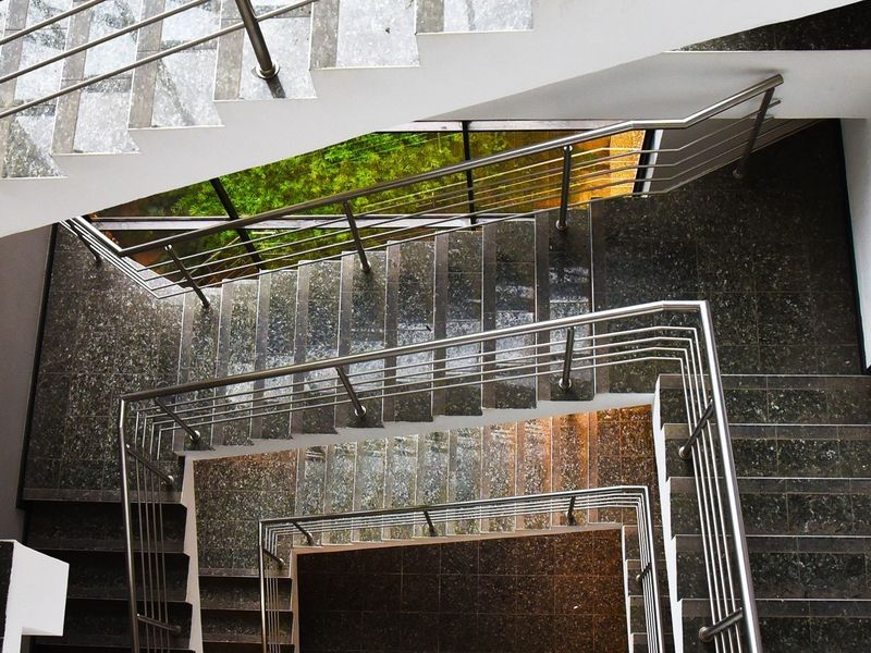A modern commercial staircase featuring polished stone steps, stainless steel railings, and a large window providing natural light.
