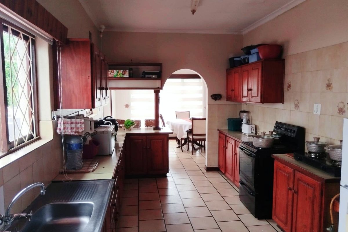 A functional kitchen featuring wooden cabinetry, tiled flooring, and a tiled backsplash, leading through an archway to the dining area.