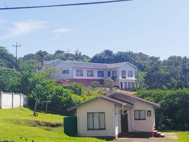 A view of the rear property elevation featuring a secondary dwelling, rainwater tank, and established garden surroundings.