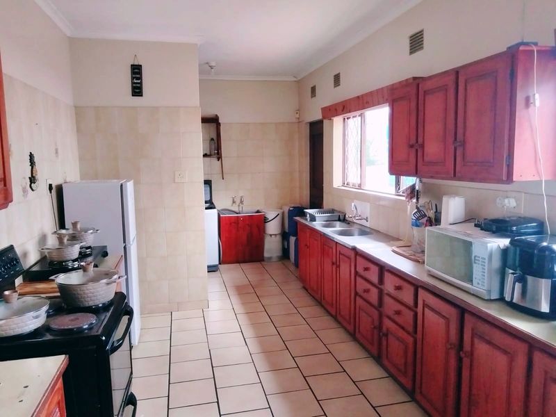 A functional kitchen featuring wooden cabinetry, tiled flooring, and a double sink with a tiled splashback.