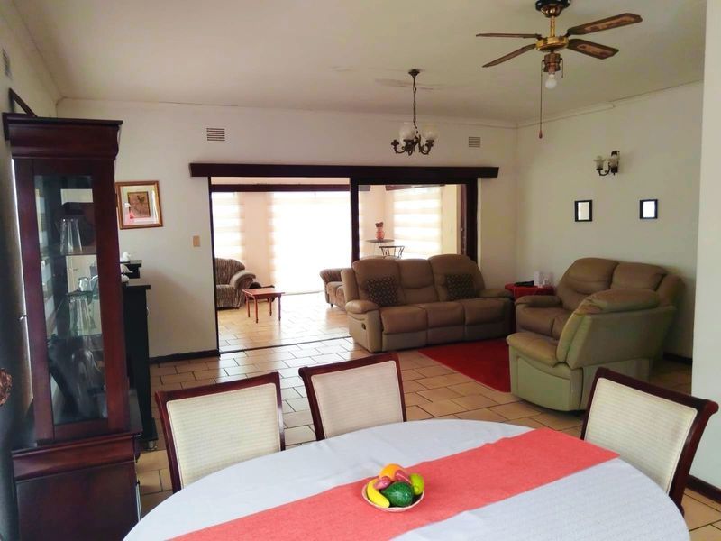 Spacious open-plan living and dining area featuring tiled flooring, ceiling fan, and large sliding doors leading to an adjacent sunroom or patio space.