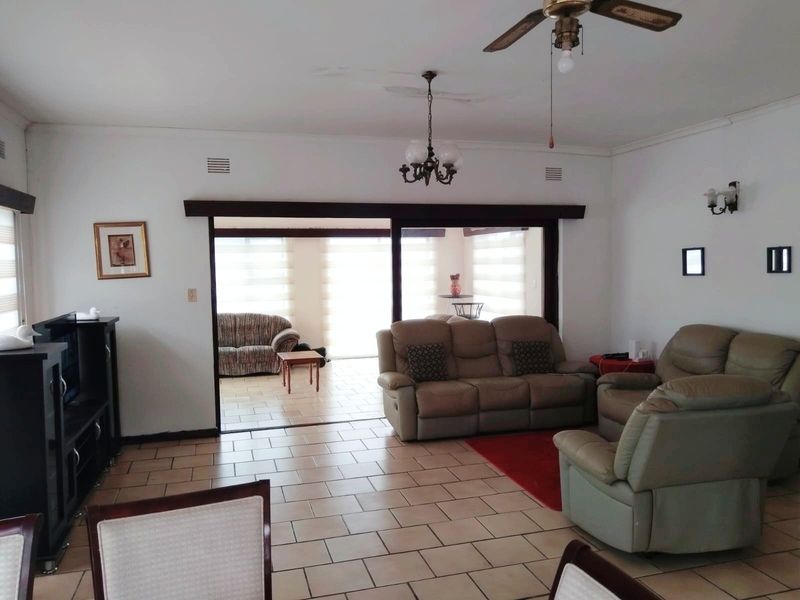 Spacious living area featuring tiled flooring, ceiling fan, and large sliding doors leading to an adjacent sunroom or patio space.