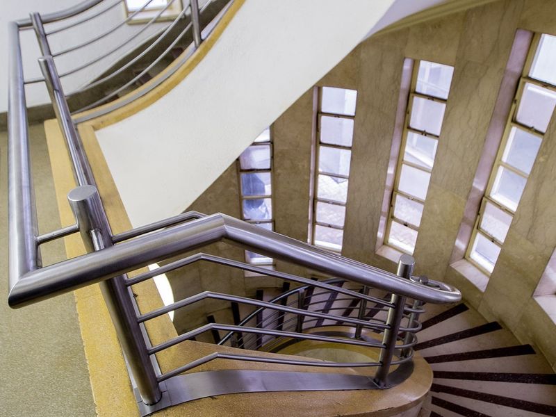 A striking curved staircase featuring stainless steel handrails and elegant stone wall cladding, illuminated by a series of vertical windows.