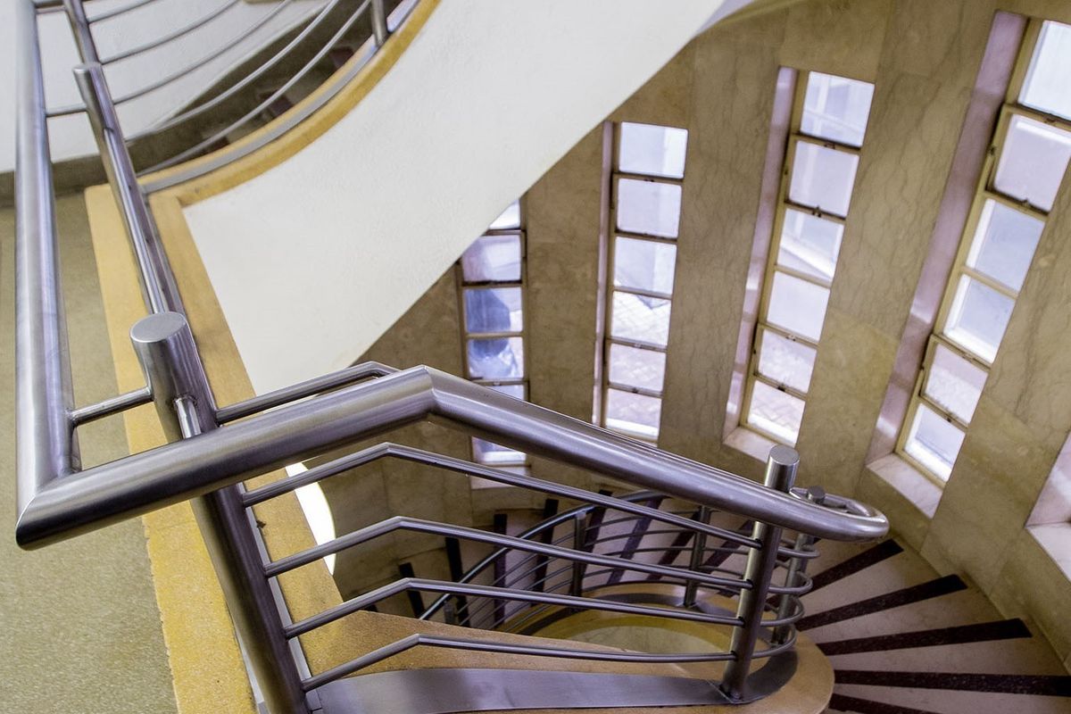 A striking curved staircase featuring stainless steel handrails and elegant stone wall cladding, illuminated by a series of vertical windows.
