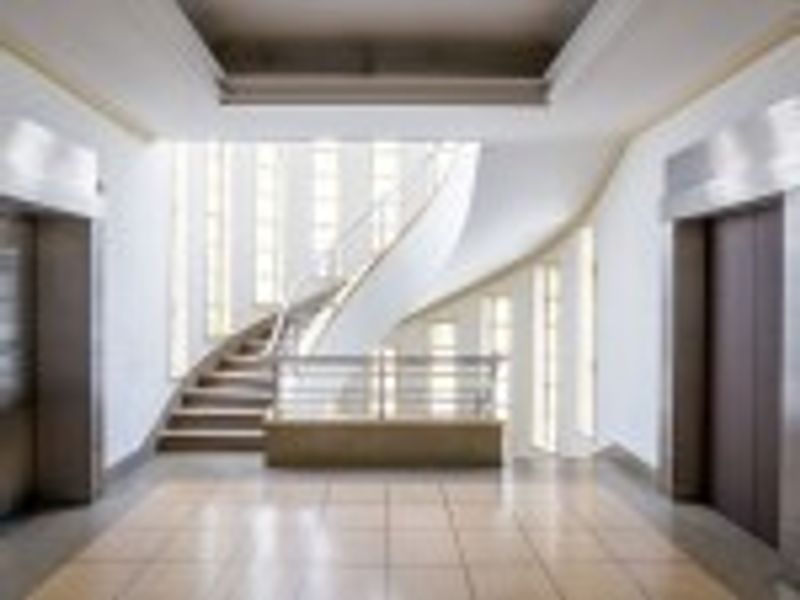 Modern commercial building entrance lobby featuring a striking curved staircase, elevator access, and polished tiled flooring with bright natural light.