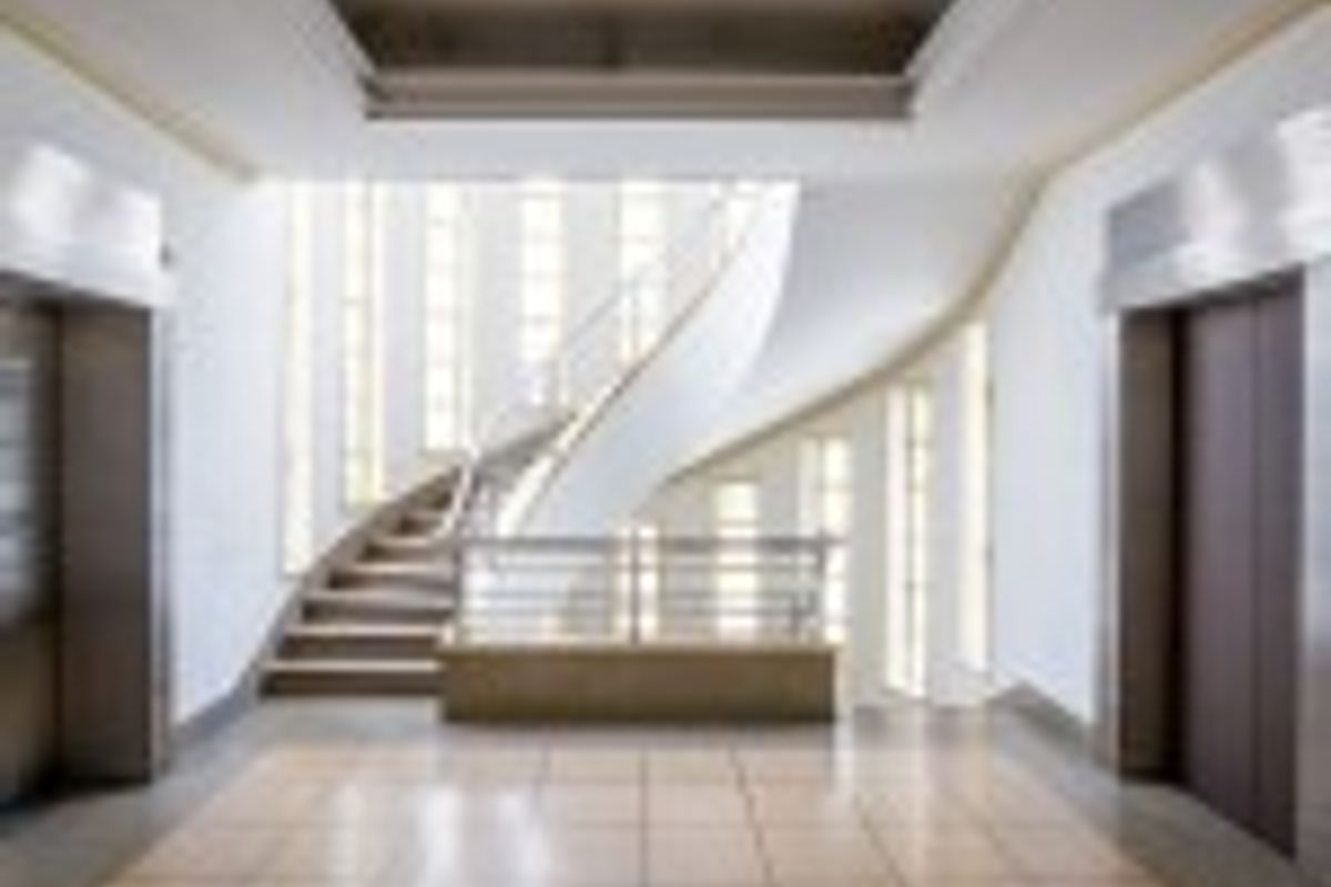 Modern commercial building entrance lobby featuring a striking curved staircase, elevator access, and polished tiled flooring with bright natural light.