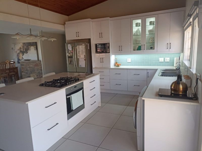 Modern kitchen featuring white cabinetry, stone countertops, a central island with a gas hob, and a stylish subway tile backsplash under a timber ceiling.