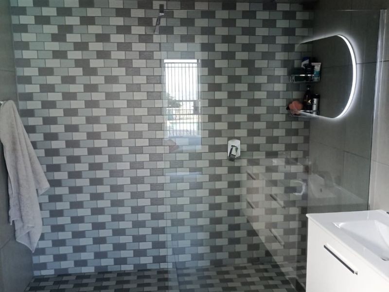 Modern bathroom featuring a spacious walk-in shower with mosaic tiling, a sleek vanity cabinet with integrated basin, and a contemporary LED backlit mirror.