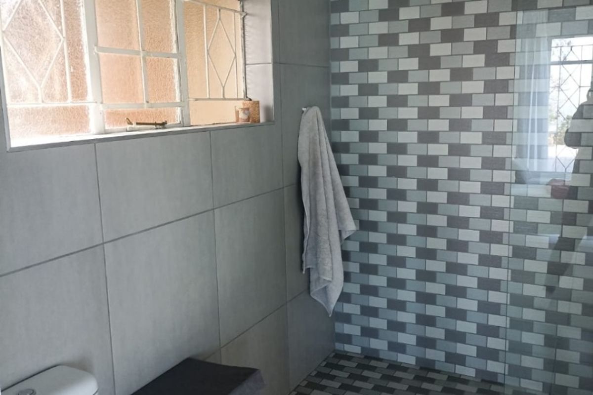 Modern bathroom featuring a walk-in shower with mosaic tile accents, large format floor tiles, and a functional toilet.