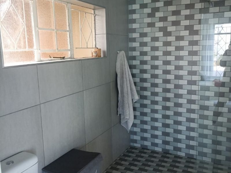 Modern bathroom featuring a walk-in shower with mosaic tile accents, large format floor tiles, and a functional toilet.