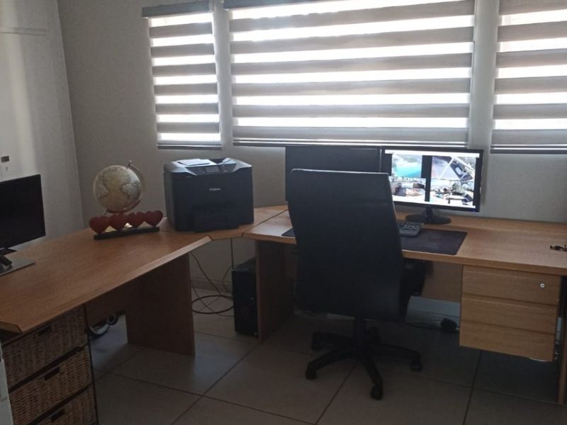 A functional home office space featuring neutral tiled flooring and modern roller blinds, providing a clean and practical environment for work.