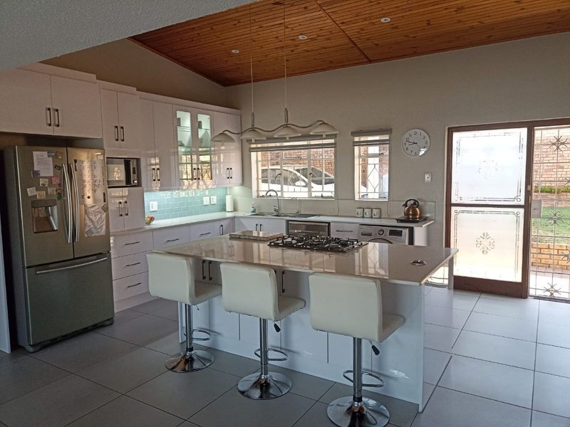 Modern kitchen featuring a central island with gas hob, sleek white cabinetry, subway tile backsplash, and a warm timber-paneled ceiling with direct garden access.