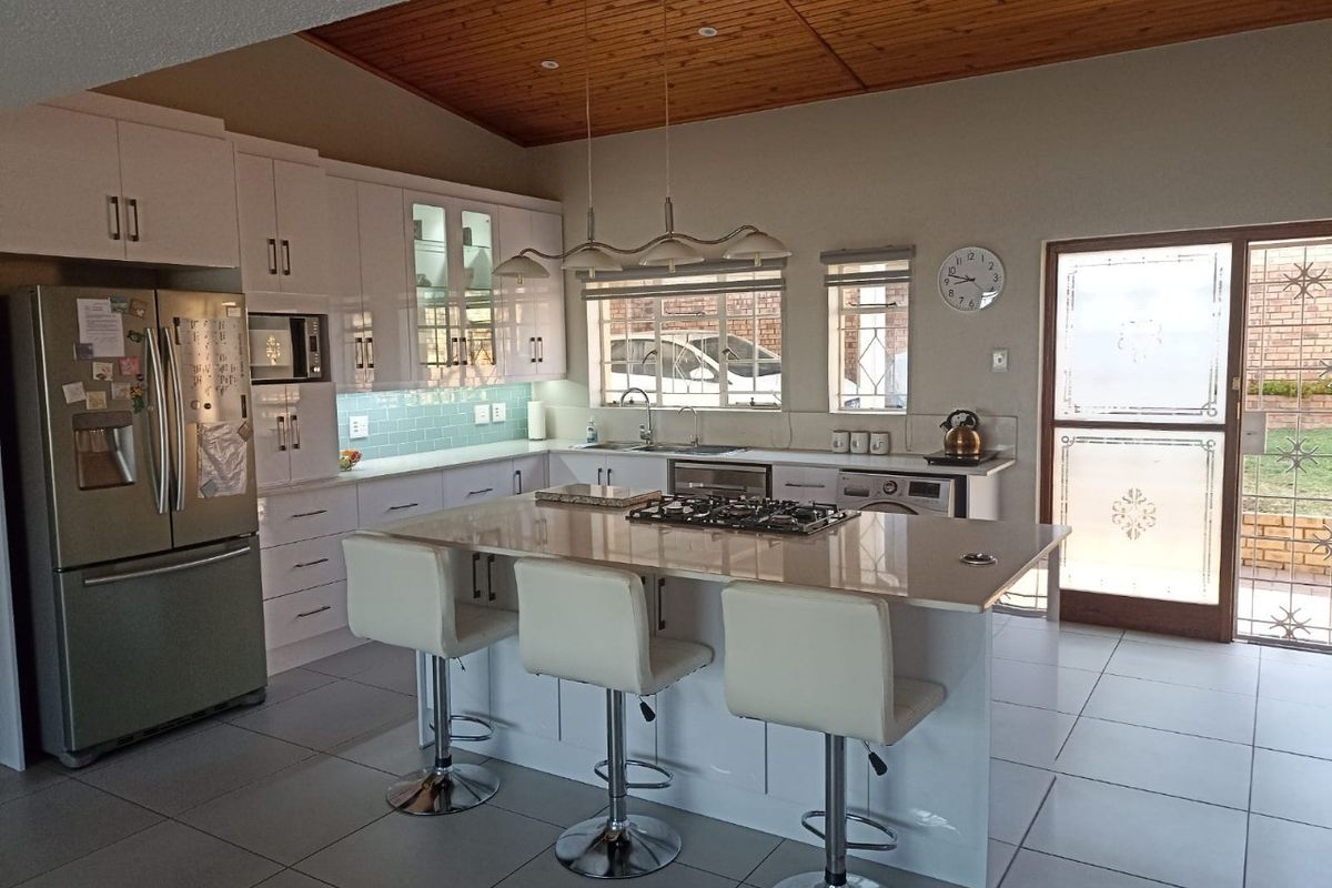 Modern kitchen featuring a central island with gas hob, sleek white cabinetry, subway tile backsplash, and a warm timber-paneled ceiling with direct garden access.