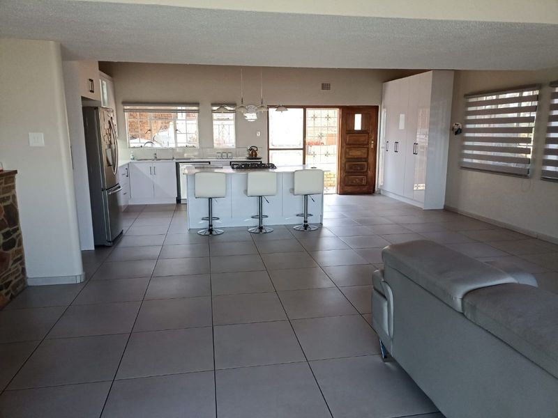 Spacious open-plan living area featuring a modern kitchen with a central island, gas hob, and ample built-in storage, finished with neutral floor tiles.