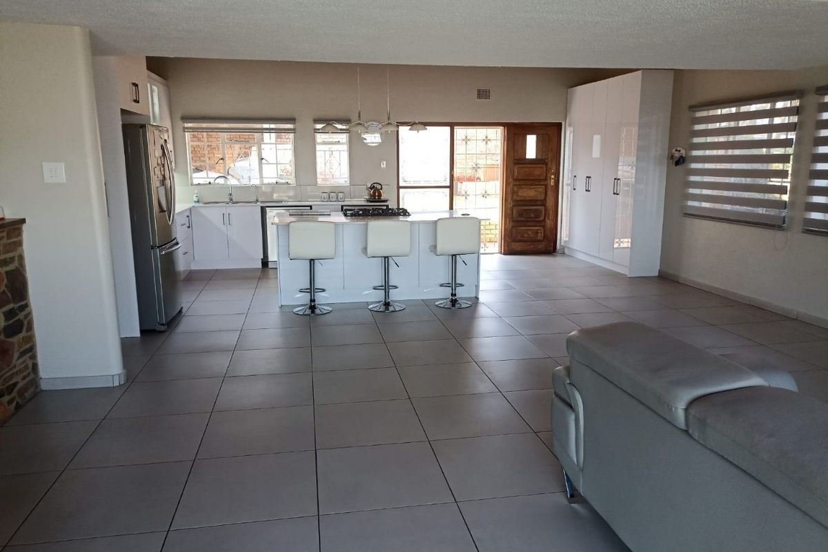Spacious open-plan living area featuring a modern kitchen with a central island, gas hob, and ample built-in storage, finished with neutral floor tiles.
