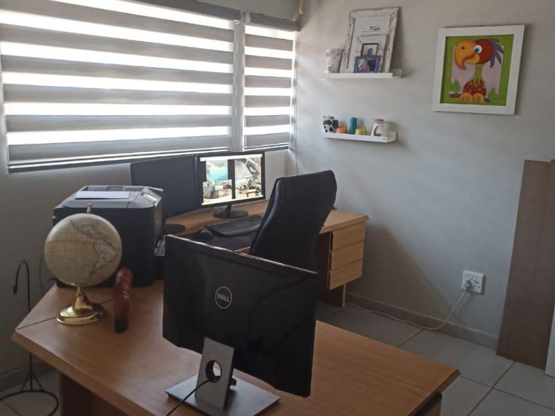 A functional home office space featuring tiled flooring, neutral wall tones, and modern dual-tone roller blinds for adjustable natural lighting.