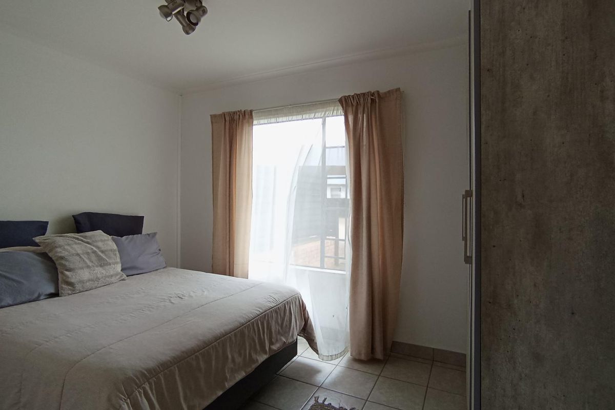 A functional bedroom featuring tiled flooring, a built-in wardrobe, and natural light through a window with curtains.