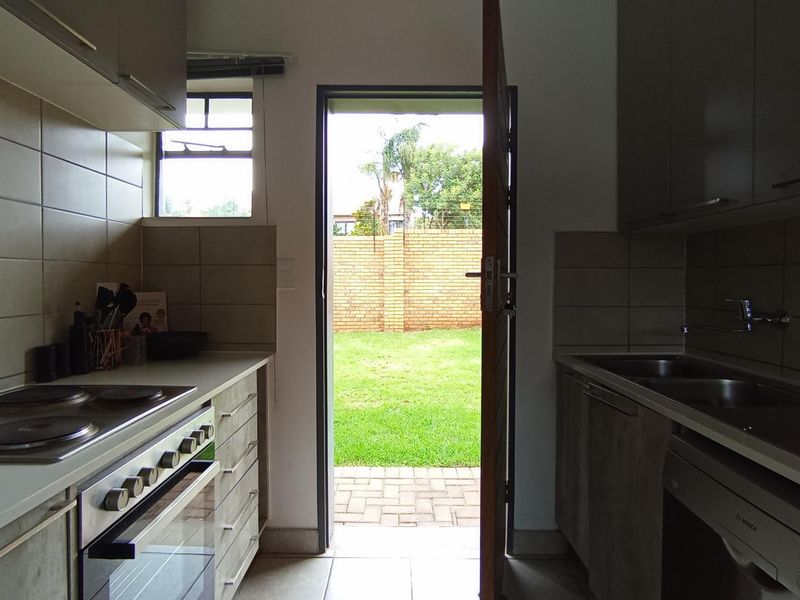 Functional kitchen featuring built-in cabinetry, electric hob, oven, and double sink, with direct access to the rear garden through an exterior door.