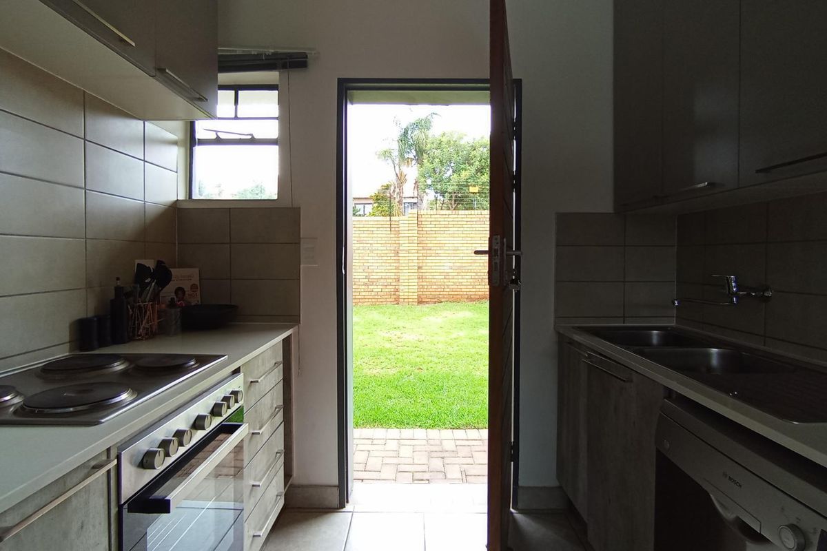 Functional kitchen featuring built-in cabinetry, electric hob, oven, and double sink, with direct access to the rear garden through an exterior door.