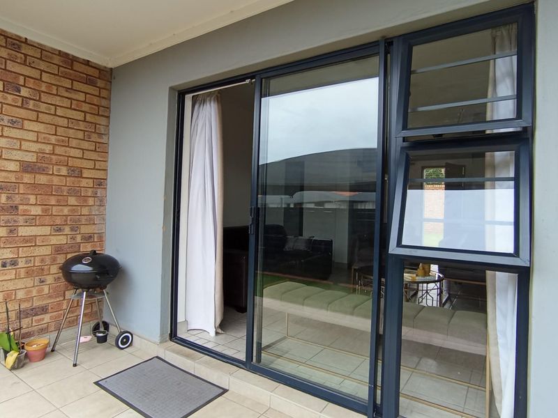 A covered patio area featuring tiled flooring, a brick feature wall, and modern dark-framed sliding glass doors providing access to the interior living space.