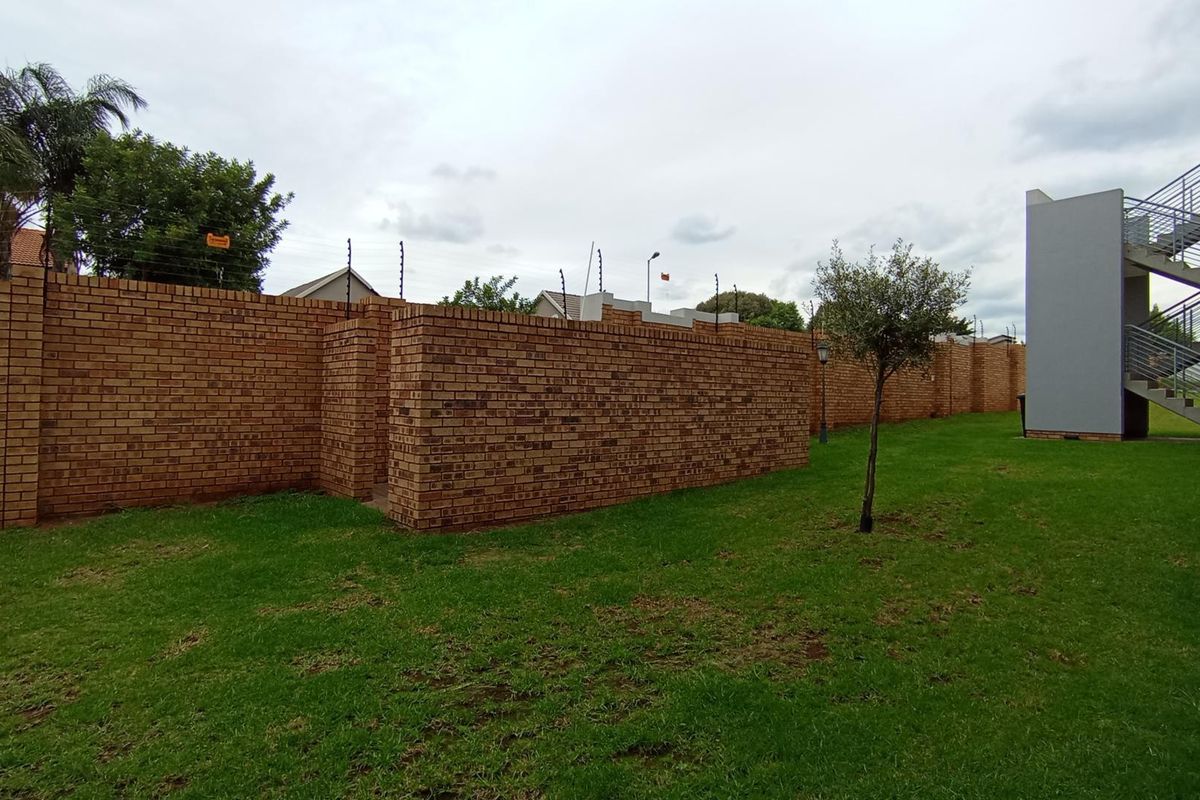 A view of the rear garden area featuring a brick boundary wall with electric fencing and an external staircase leading to upper levels.