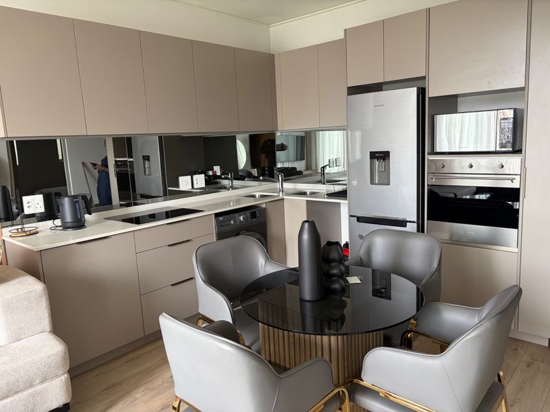 Modern open-plan kitchen featuring sleek taupe cabinetry, integrated appliances, a mirror splashback, and a seamless transition to the dining area.