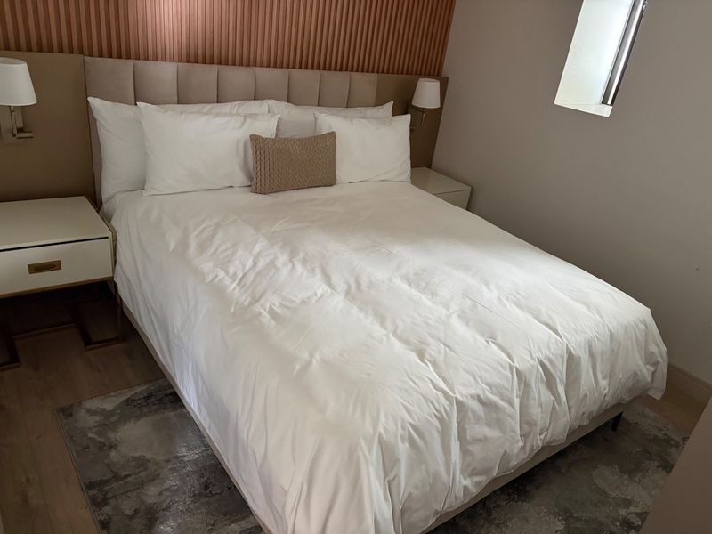 A well-appointed bedroom featuring a modern upholstered headboard, decorative slatted wall paneling, and integrated wall-mounted lighting fixtures.