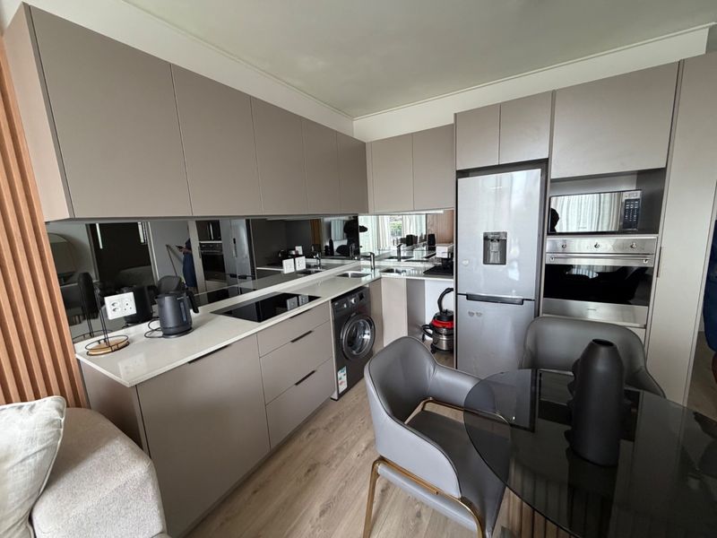 Modern open-plan kitchen featuring sleek handleless cabinetry, stone countertops, a mirrored backsplash, and integrated appliances including an oven, microwave, and washing machine.