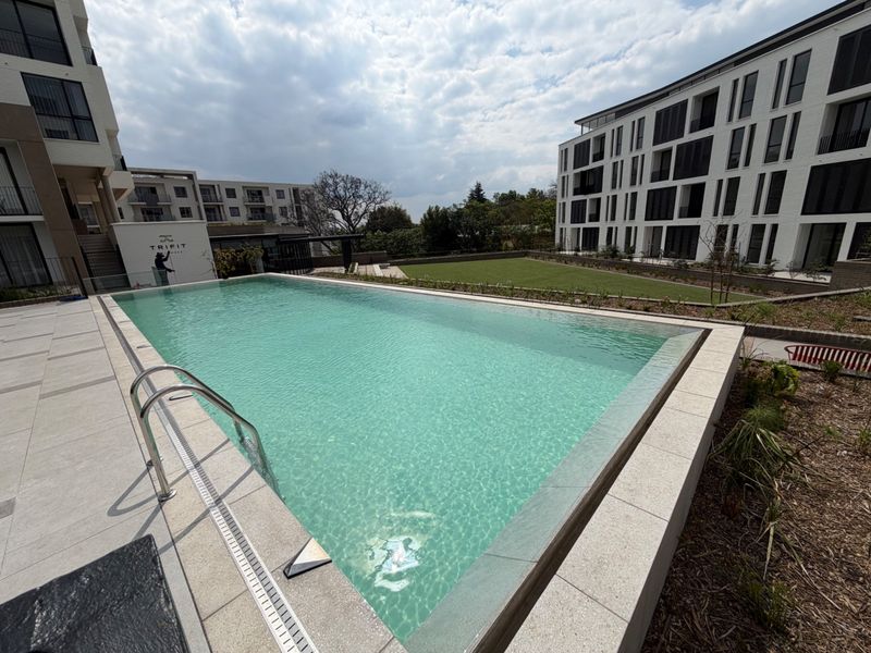 A modern, well-maintained swimming pool area set within a contemporary apartment complex, featuring paved decking and landscaped surroundings.