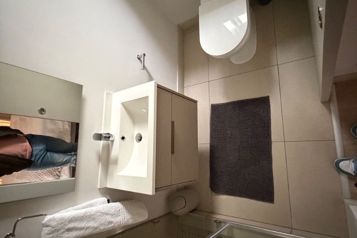 A compact bathroom featuring a wall-mounted vanity with integrated basin, a modern toilet, and a glass-enclosed shower area with neutral floor tiling.