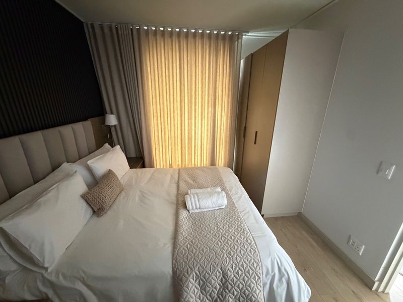 A well-maintained bedroom featuring built-in wardrobes, modern slatted wall paneling, and light laminate flooring with floor-to-ceiling curtains.