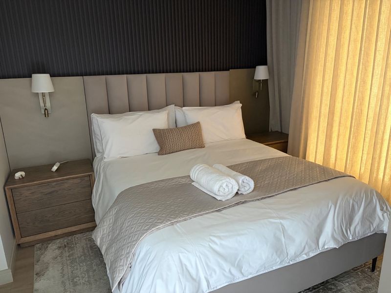 Modern bedroom featuring a stylish upholstered headboard, integrated bedside cabinetry, and elegant wall-mounted lighting against a textured feature wall.