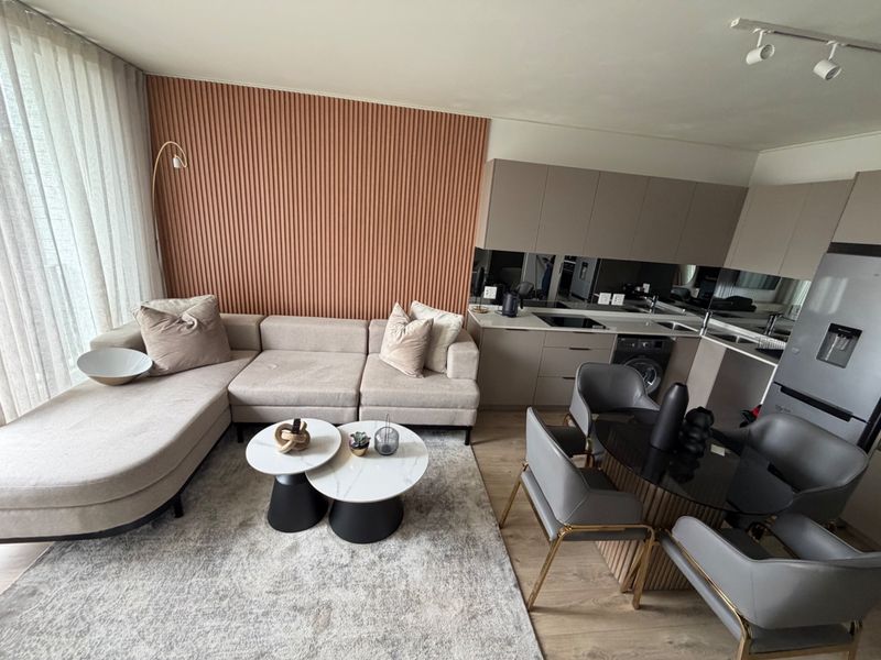 Modern open-plan living area featuring a sleek kitchen with integrated appliances, a stylish slatted feature wall, and contemporary finishes throughout.